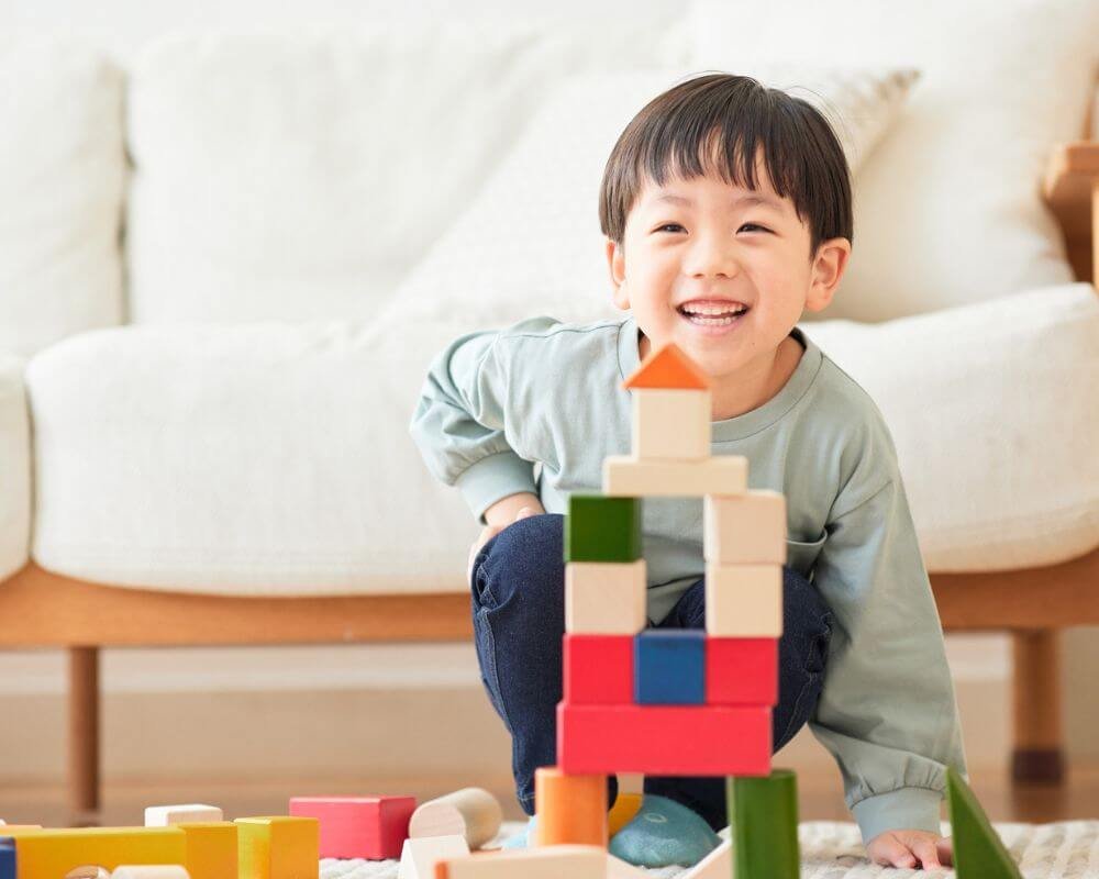 Een erg blij kind dat opgewonden lacht nadat het een spel heeft voltooid waarbij het kleine speelblokken op elkaar stapelde om een structuur te bouwen